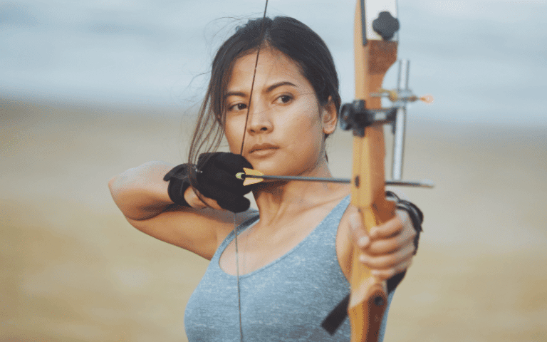 Women in archery, aiming bows at targets in a forest clearing