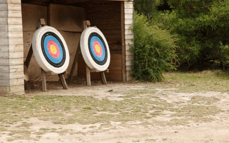 An outdoor archery range with safety barriers, clear signage, and designated shooting lanes. Safety equipment such as arm guards and finger tabs are visible