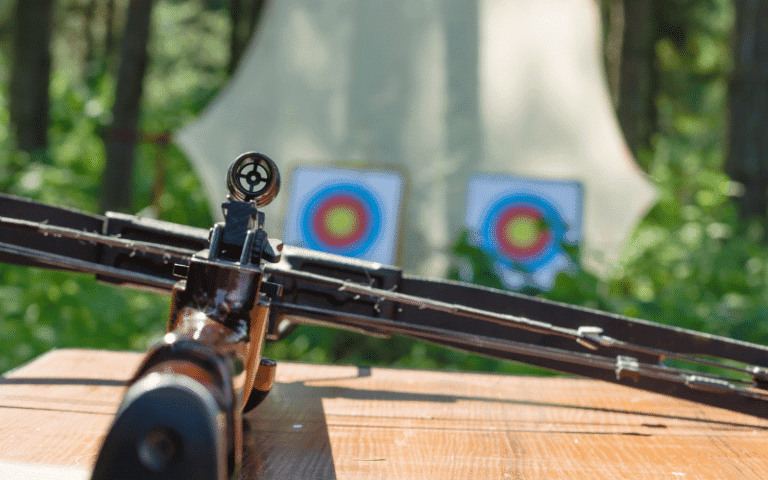 A bow and arrow resting on a wooden table, surrounded by targets and archery equipment