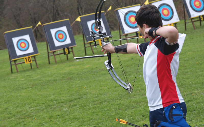 A bow and arrow are set up on a target in a beginner's archery class. The instructor demonstrates proper technique