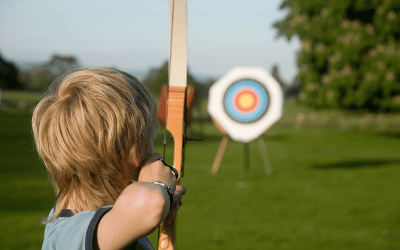 Children and teenagers learning the basics of archery in a peaceful outdoor setting