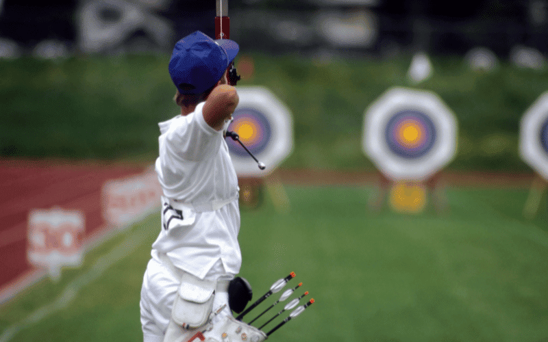 A bustling archery competition with cheering crowds and colorful targets set against a scenic backdrop