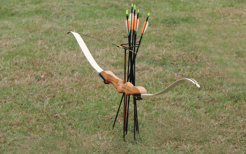 A bow and arrow set up on a target range, with various training equipment and plans for advanced shooting techniques displayed nearby