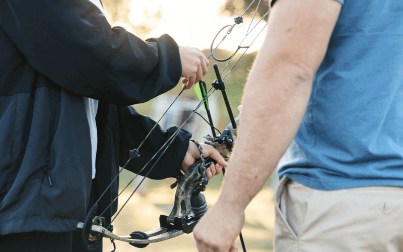 A bow and arrow are set up on a shooting range, with safety equipment and guidelines for injury prevention displayed nearby